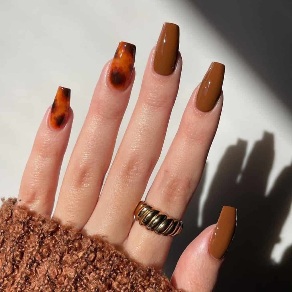 A woman's hand with long coffin-shaped nails painted predominantly in a striking brown