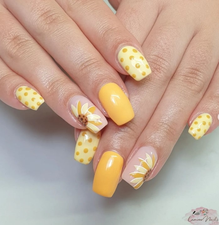 A woman's hand with deep yellow nails mixed with light yellow nails decorated with dark yellow polka dots
