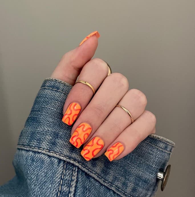 A woman holding a light orange nails with deep orange blob outlines on each nail