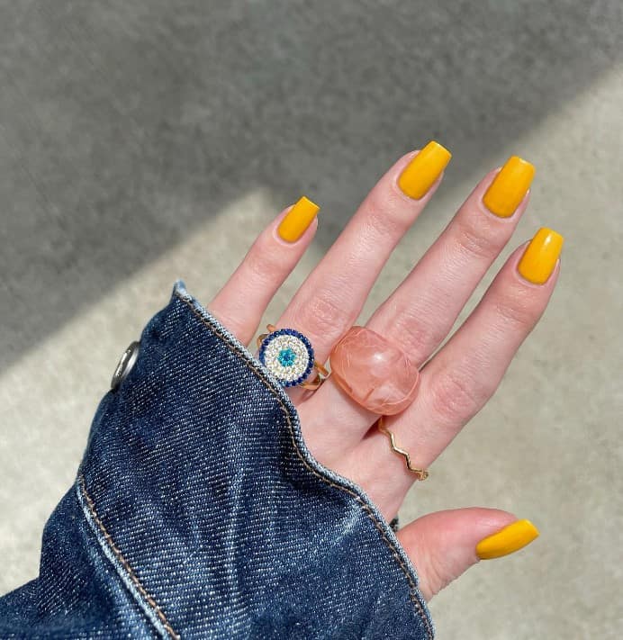 A woman with mustard-colored square nails and denim jacket.