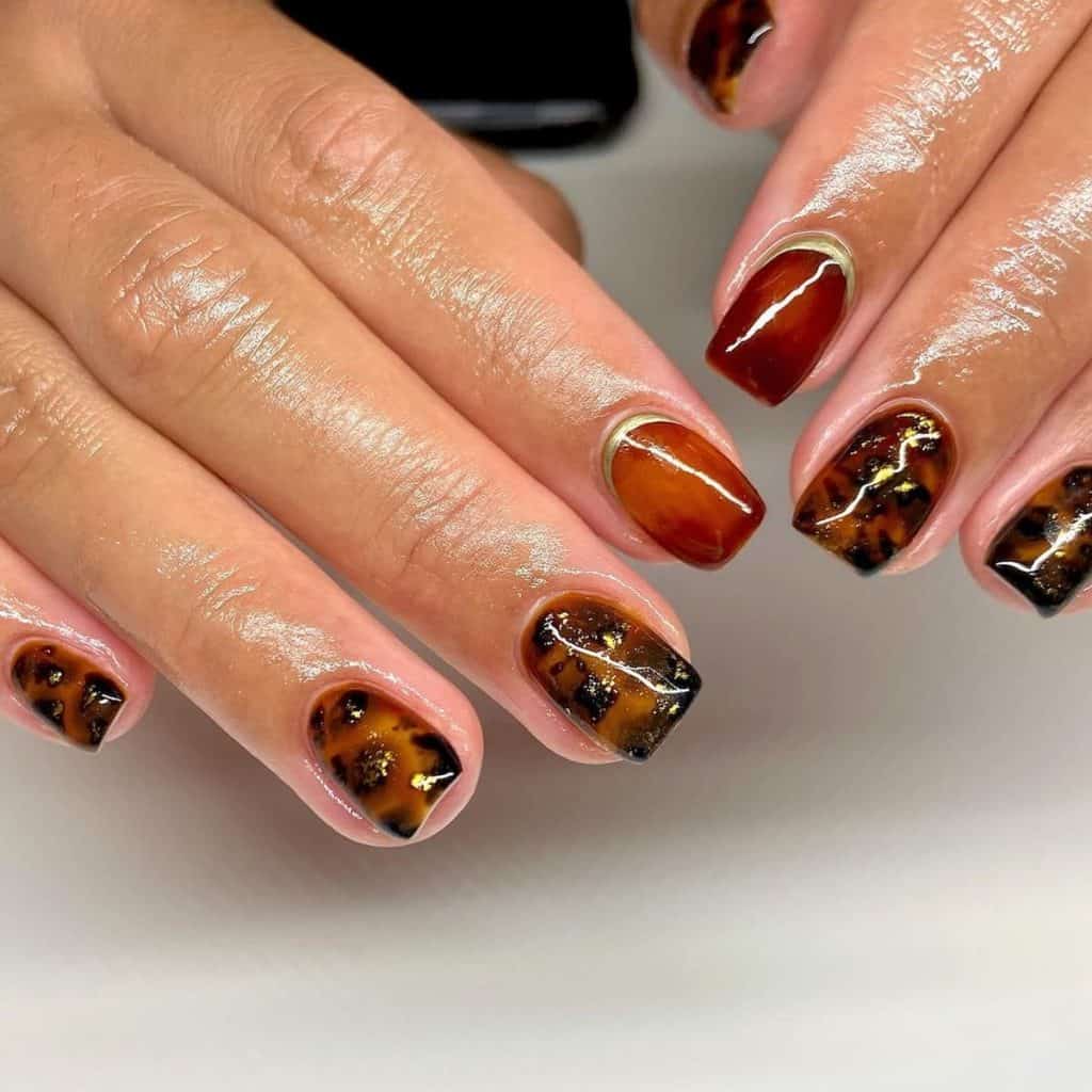 A woman's nails with one in a rich brown with chrome gold reverse French tips and the other with a more mottled pattern with gold flakes