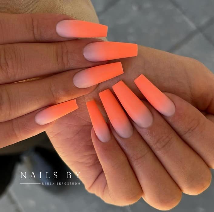 A woman's long coffin nails feature a stunning light orange and pale pink gradient