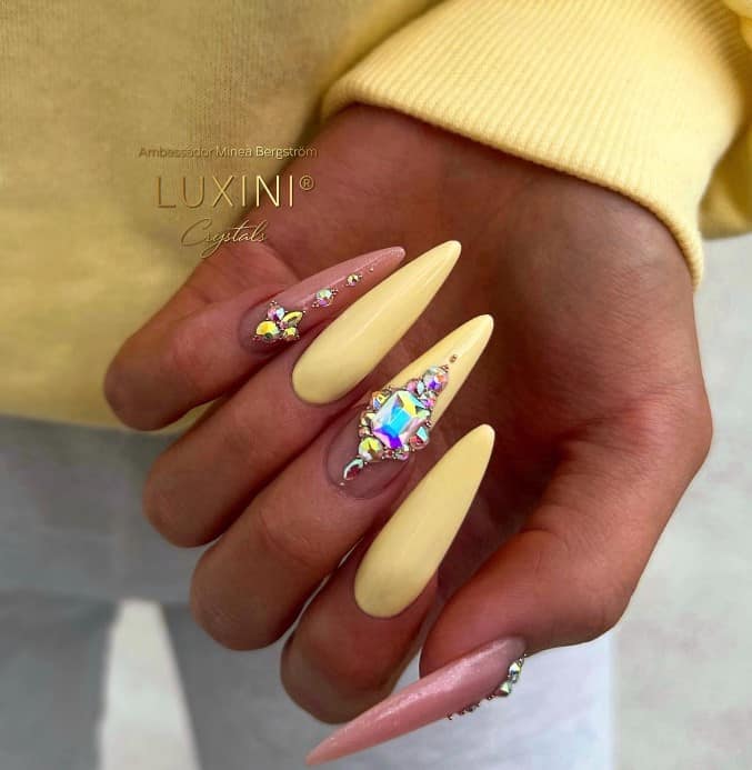 A woman's nails with deep pink and yellow nails highlighted by a deep French tip and intricate rhinestone nail gems trickling down the nails