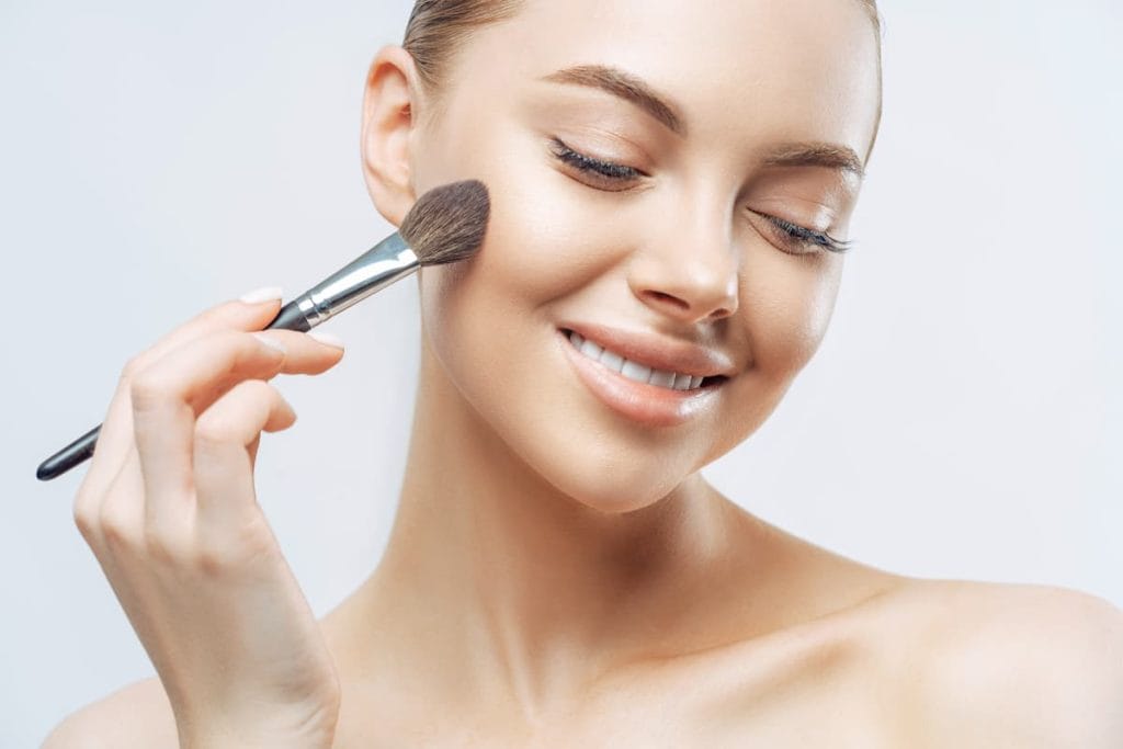 a young woman applying the missha bb cream using a brush while smiling