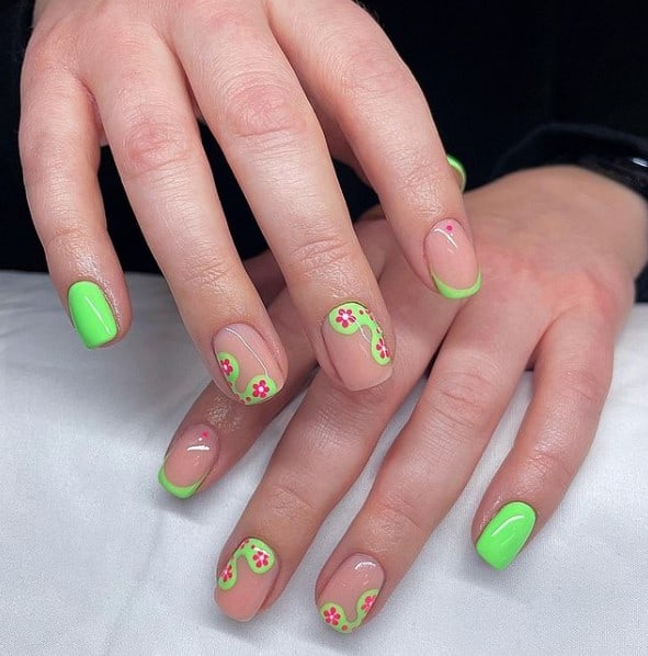A woman's hands with nude base to three nails and a neon green polish to create blobs on the edges of two nude nails, and paint magenta flowers on top of the blobs.