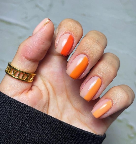 A woman's hand with several shades of orange on your nails in a unique way with this fun half-and-half mani.