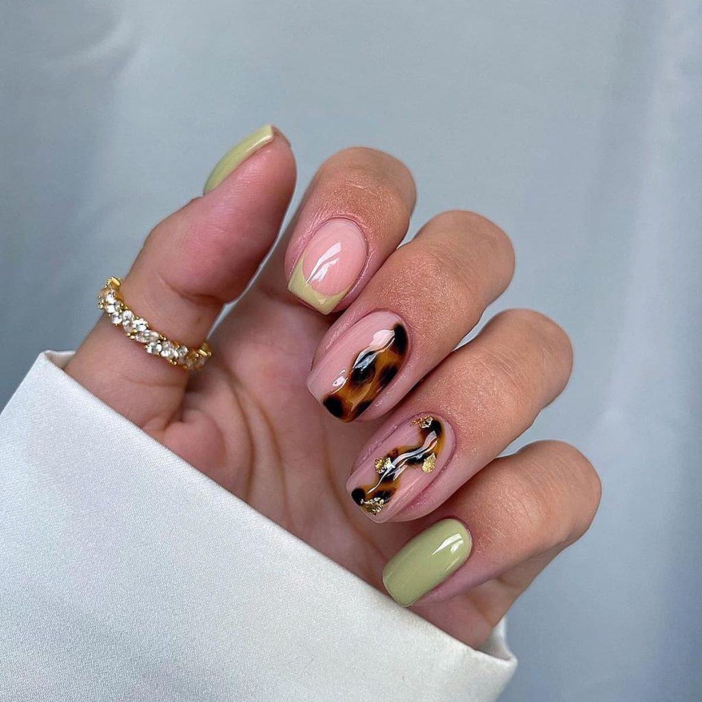 A woman's hand with a glossy nail set pairs tortoiseshell patterns with green accents, including one nail with a green French tip