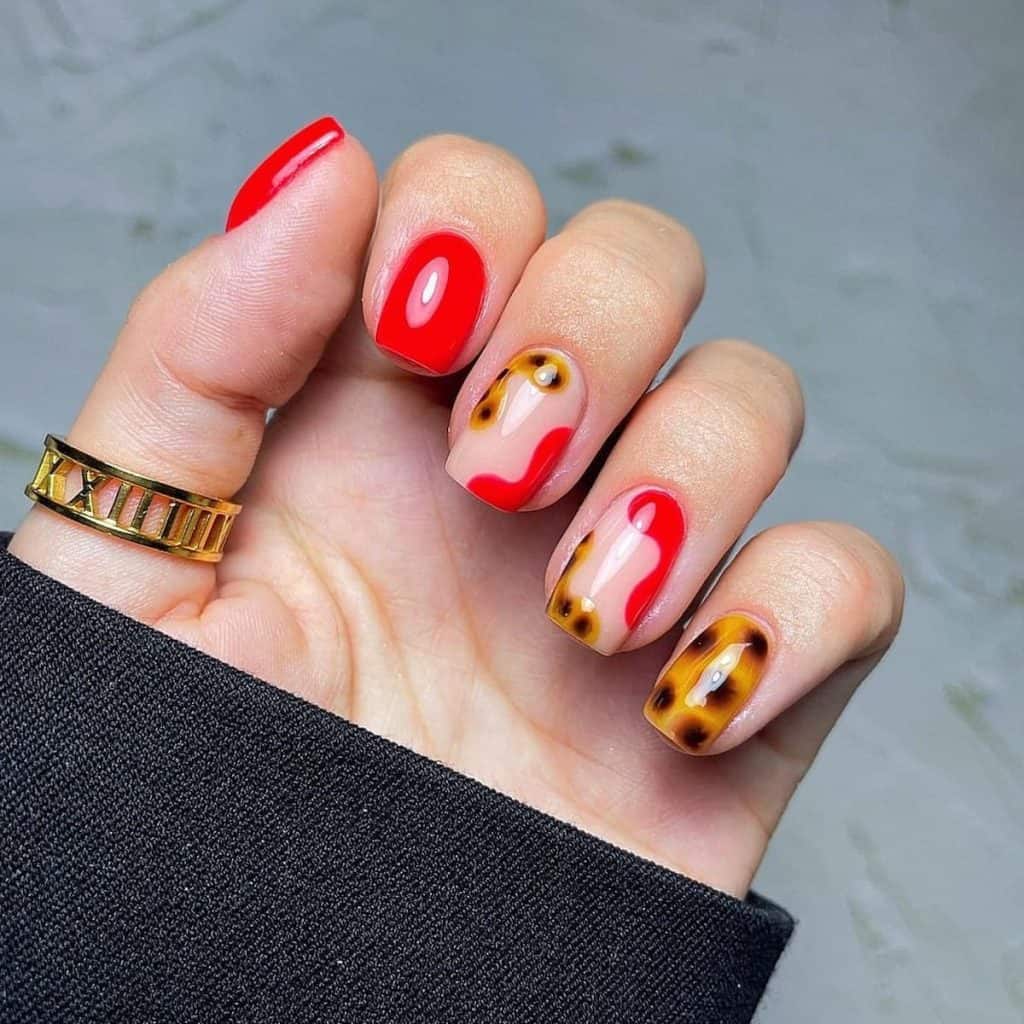 A woman's hand holding gel tortoiseshell nails — vibrant red intertwining with tortoiseshell in a daring dance of color, revealing the understated charm of a nude base