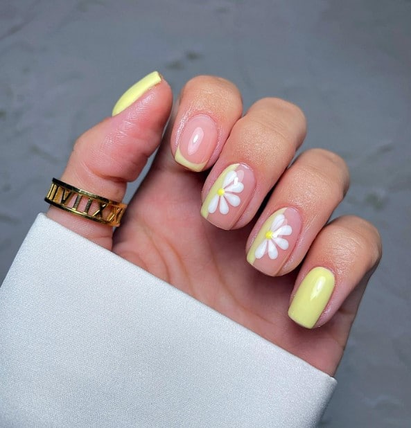 A woman's hand holding a pale yellow nail design and features nude accent nails with yellow French tips and large half daisies with thick yellow lines at the sides
