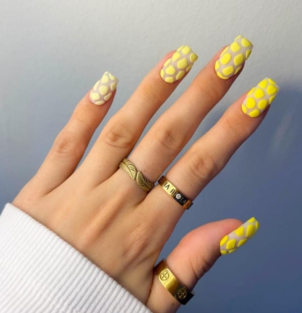 A woman's hand with light yellow base and dot it all over with geometric shapes that steadily get darker to create a textured 3D mosaic effect