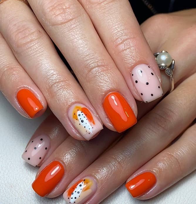 A woman's hand features bright orange nails and two pretty accent nails