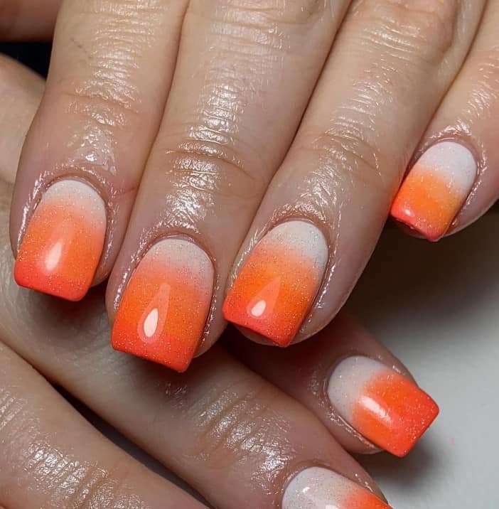 A woman's hands with each nail goes from nude to light orange to deep orange, topped off with a gold glitter finish