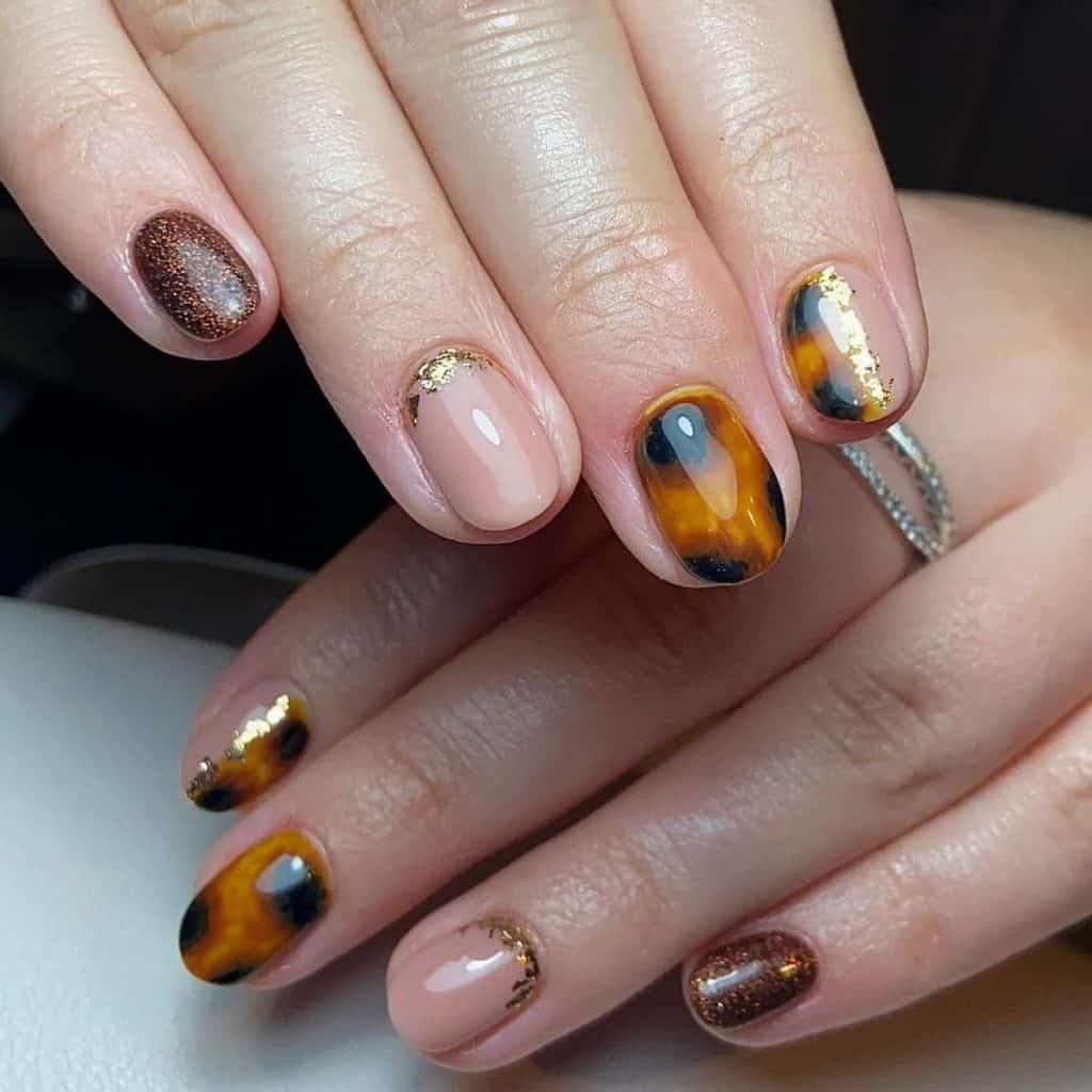 A woman set of nails with varied designs: paint one in a shimmering brown, another in a nude shade featuring golden reverse French tips, and a third showcasing a tortoiseshell pattern
