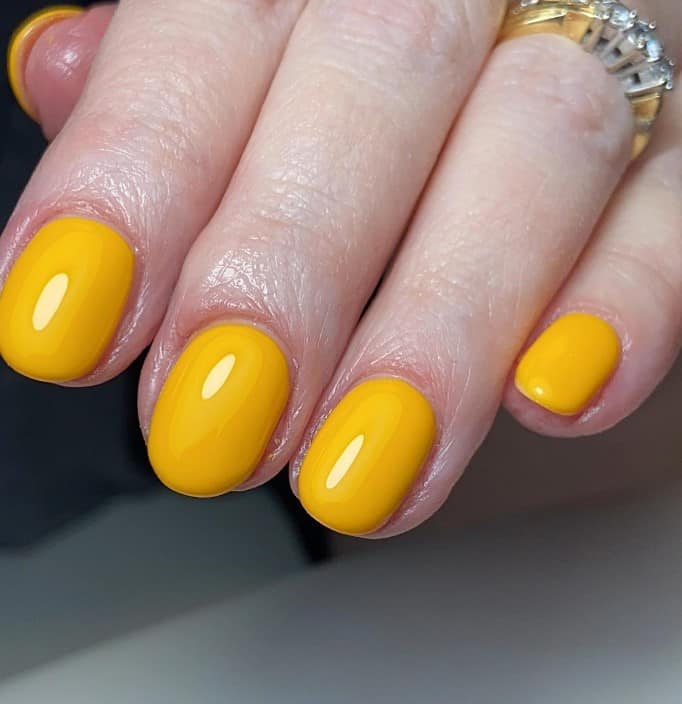 A woman's hand features deep yellow round nails topped off with a glossy topcoat