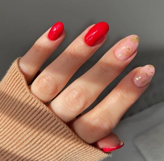 A woman's hand with red and nude nails with gold foils.
