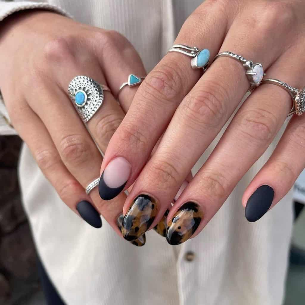A woman's hand with plain matte black nails and sophisticated French tips with sleek, glossy tortoiseshell patterns