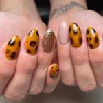 A woman's hands with tortoiseshell nail patterns in orange, interplaying with opulent gold glitter and soothing nude brown