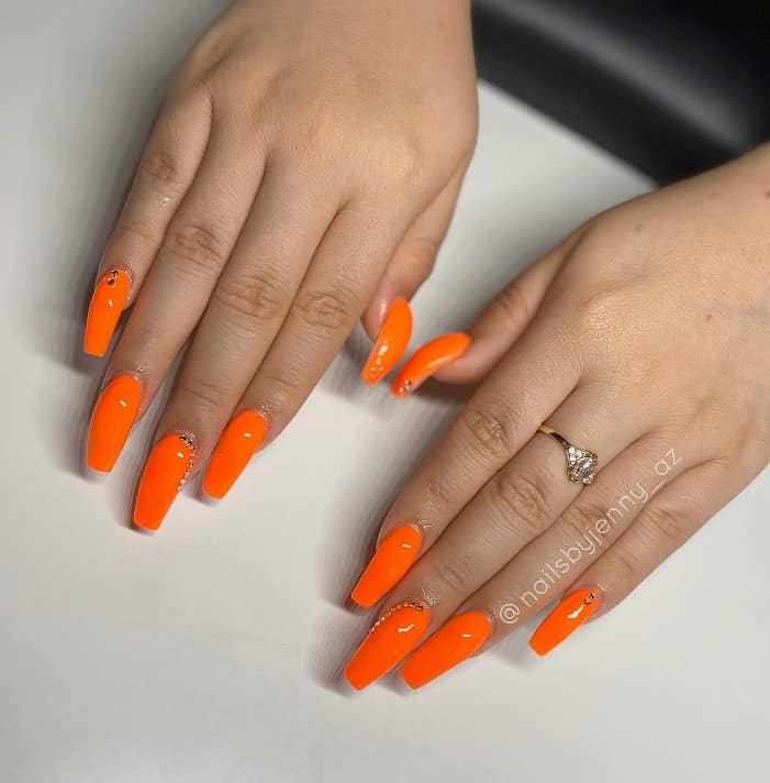 A woman's hands with vibrant orange ballerina-shaped nails adorned with silver gems
