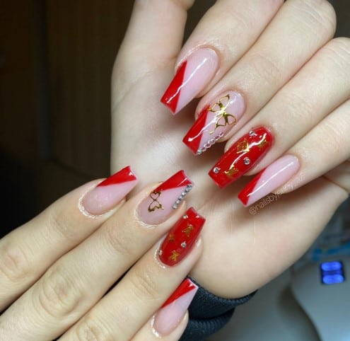 A woman's hand with red, pink nails with gold accents.