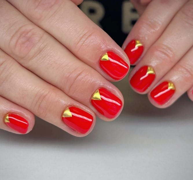 A woman's hands with red nails and triangle gold accents.