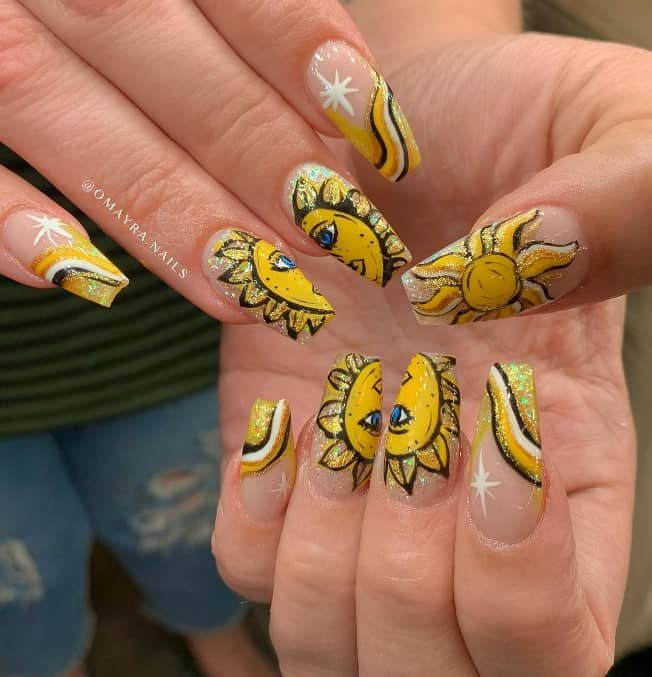 A woman's nails are decorated with splendid and intricate glittery half suns on the middle nails, with yellow, white, and black wavy glitter French tips and white starbursts