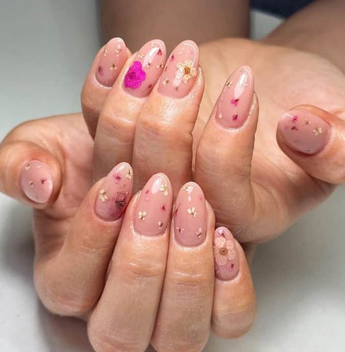 A woman's hands with nude nail in this design showcases hot pink, white, and mauve dried flowers
