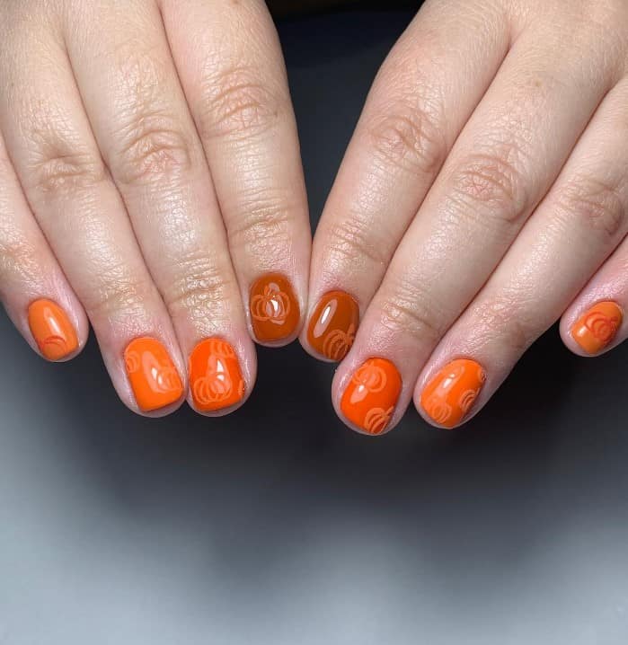A woman's hands with warm orange and brown colors and decorate them with velvet pumpkins nails.