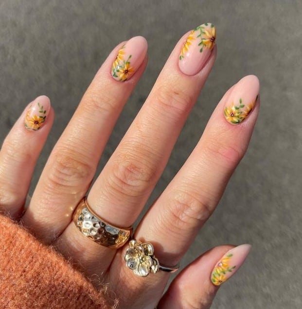 A woman's nude nails bloom into a meadow of sunshine with delicate yellow flowers and green foliage sprouting from the cuticles