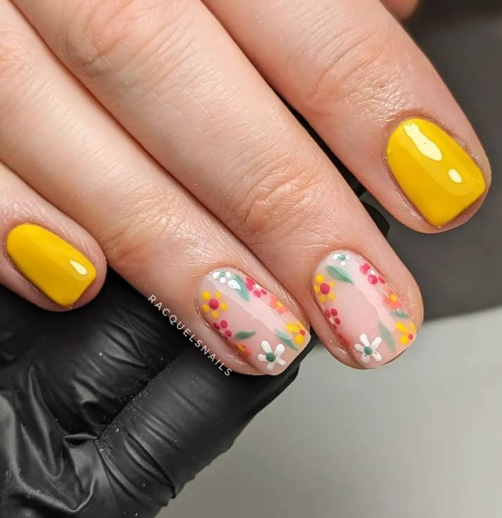 A woman's hand with mustard square nails mix with nude nail accents painted with flowers in various colors like orange, white, red, and mustard and green leaves
