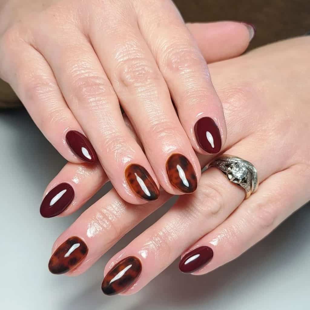 A woman's hands with red tortoiseshell nails that pair the deep allure of merlot with the intricate detail of tortoiseshell, all sealed with a glossy finish