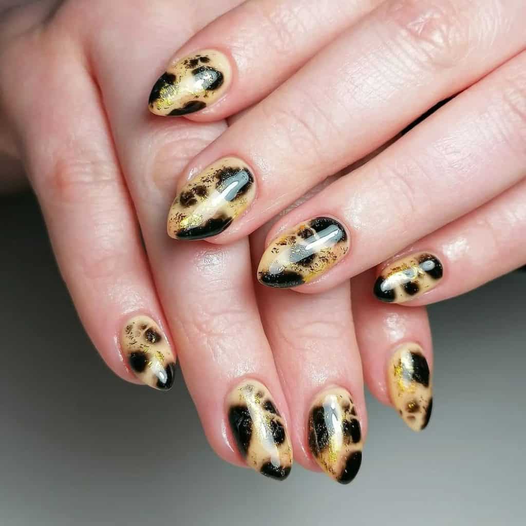 A woman's almond-shaped nails feature a shimmering pattern with flecks of gold foil for added dazzle with a leopard print design.