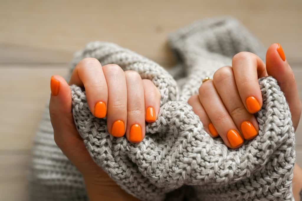 A woman's hands with orange nails holding a sweater.
