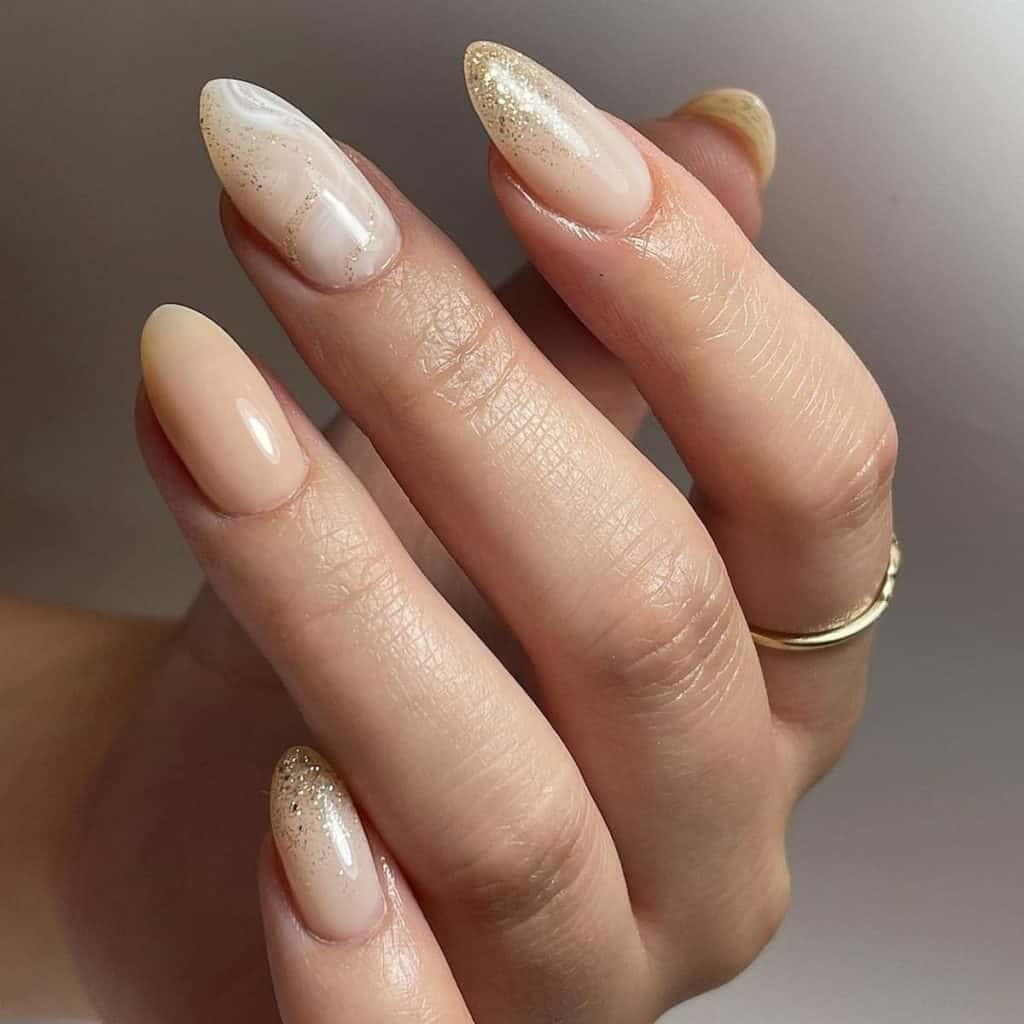 A woman's hands with almond aesthetic nails boast a subtle charm, with a nude canvas delicately decorated with swirls of white and gold glitter