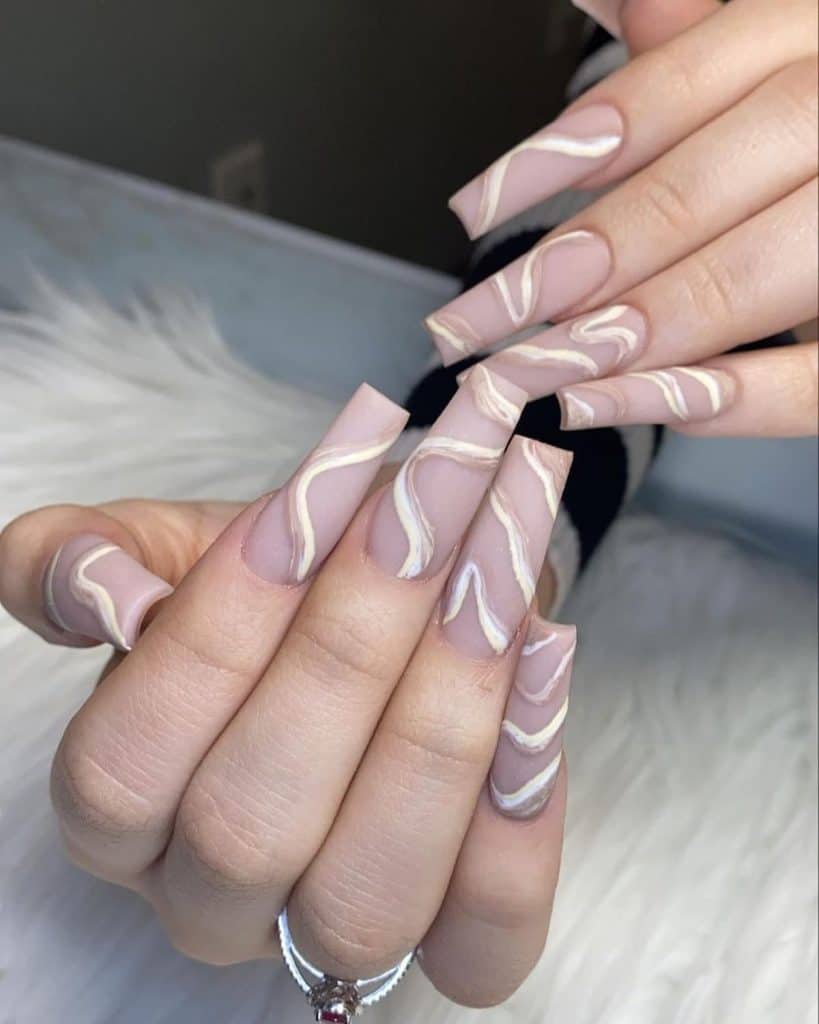 Long square nails coated in a cool nude hue come alive with white and light brown swirls