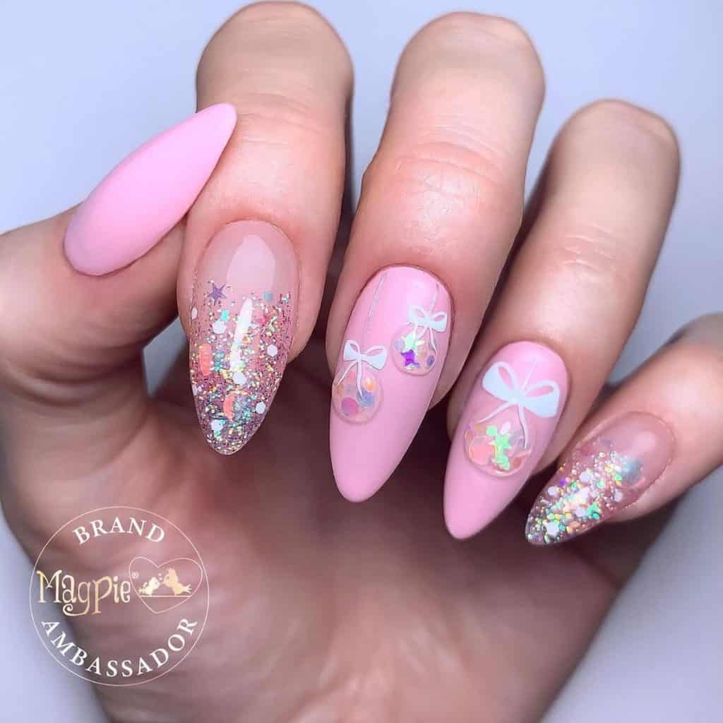 A woman's clear and pink matte nails that twinkle like Christmas lights, featuring bauble art and glossy nails that fade from starry glitter tips to a clear color toward the cuticles.