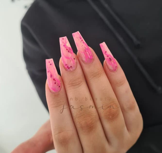 A woman showcasing her nails where a translucent pink kisses your nails, embracing swirls of deeper pink and winks of chunky glitter