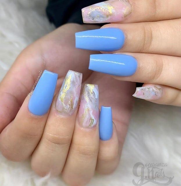 A woman's hand showcasing stunning coffin nails adorned with blue and gold marbling.