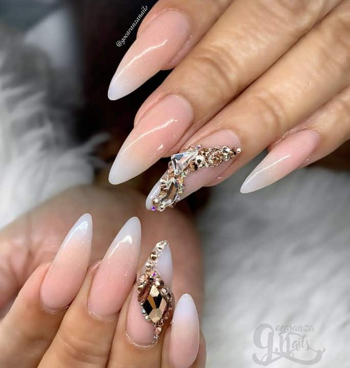 Glossy nude to white ombré nails are subtly sprinkled with glitter, while accent nails are crowned with large rose gold gems