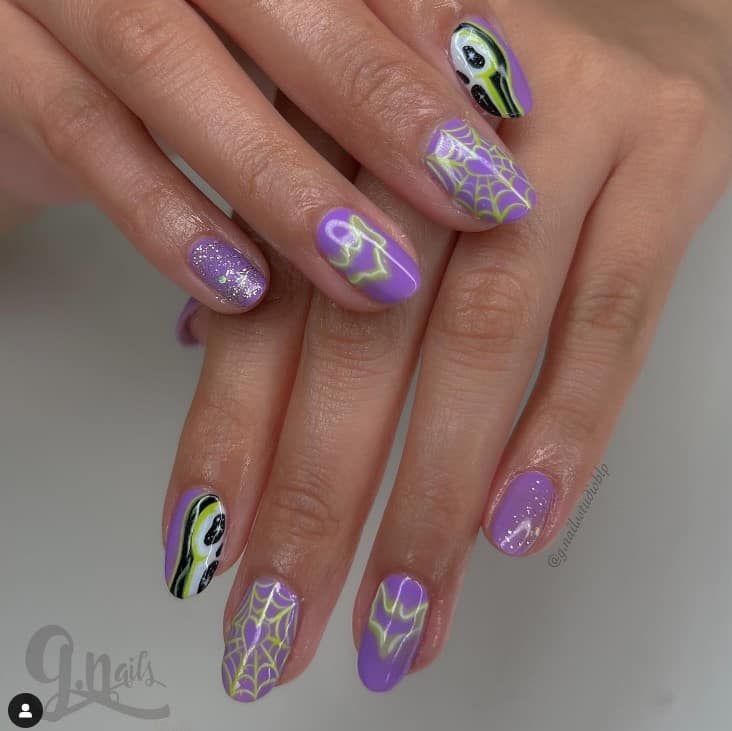 Short lavender spiderweb nails bring on the Halloween vibe with pale lime, white, and black designs.
