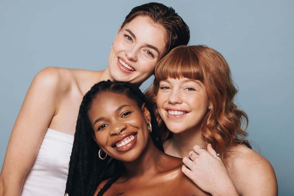 Portrait of women with different skin tones smiling at the camera in a studio.
