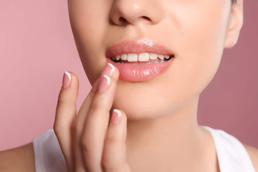 A woman is touching her lips on a pink background.