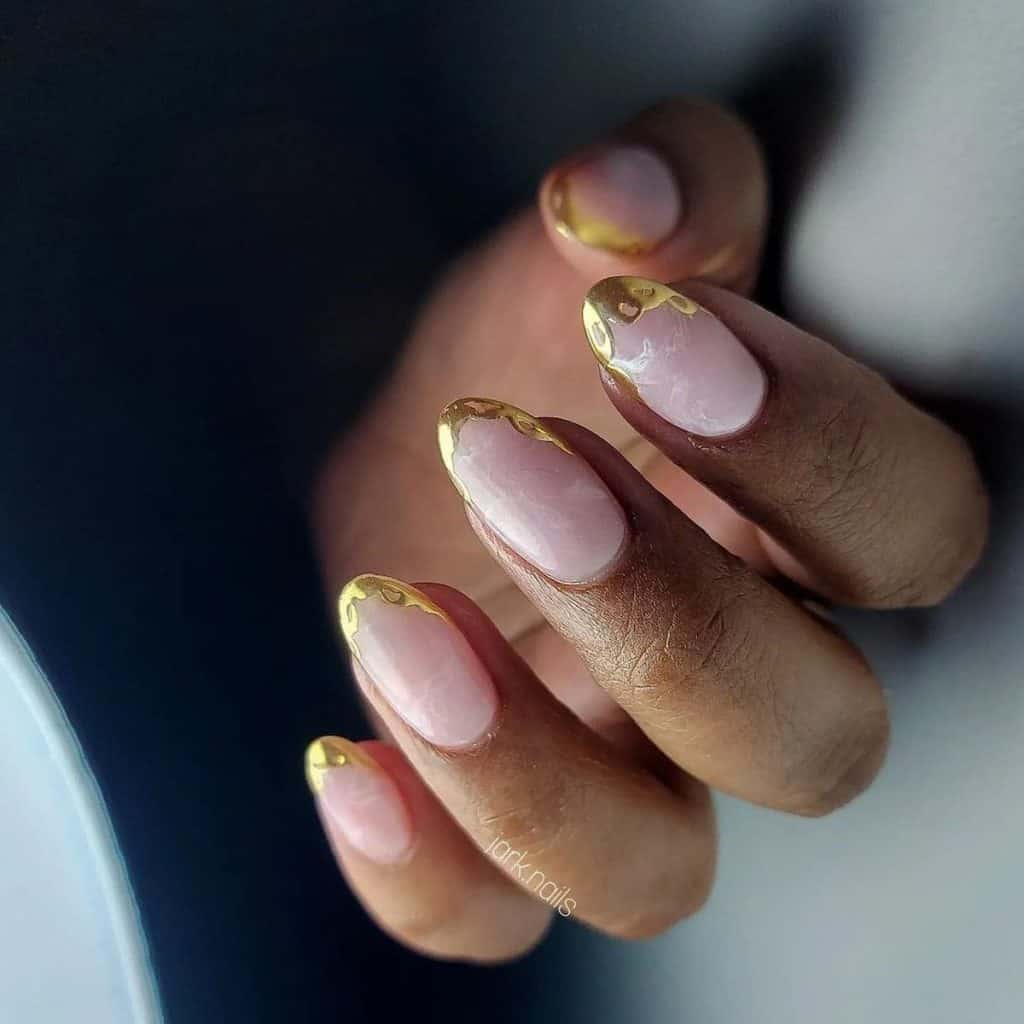 A woman's hand holding a aesthetic nude nails are a nod to classic beauty, edged with intricate gold chrome doily-like patterns that speak of timeless sophistication with a golden whisper