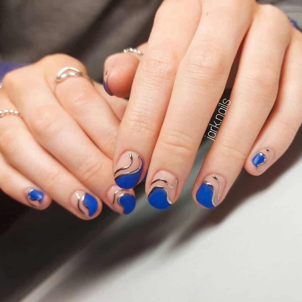 Short matte nude nails are graced with blobs of royal blue outlined with platinum polish near the tips. 