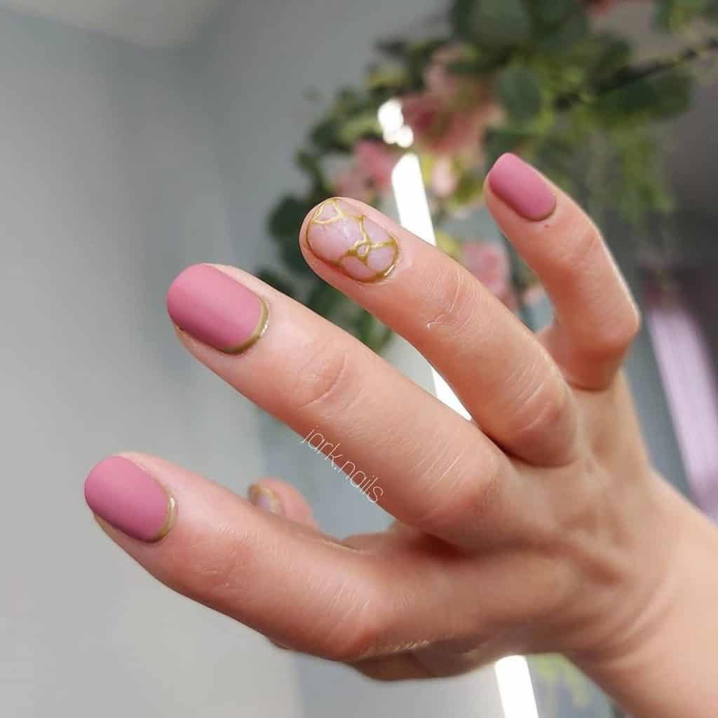 A woman's old rose nails, each adorned with a bronze reverse French tip.