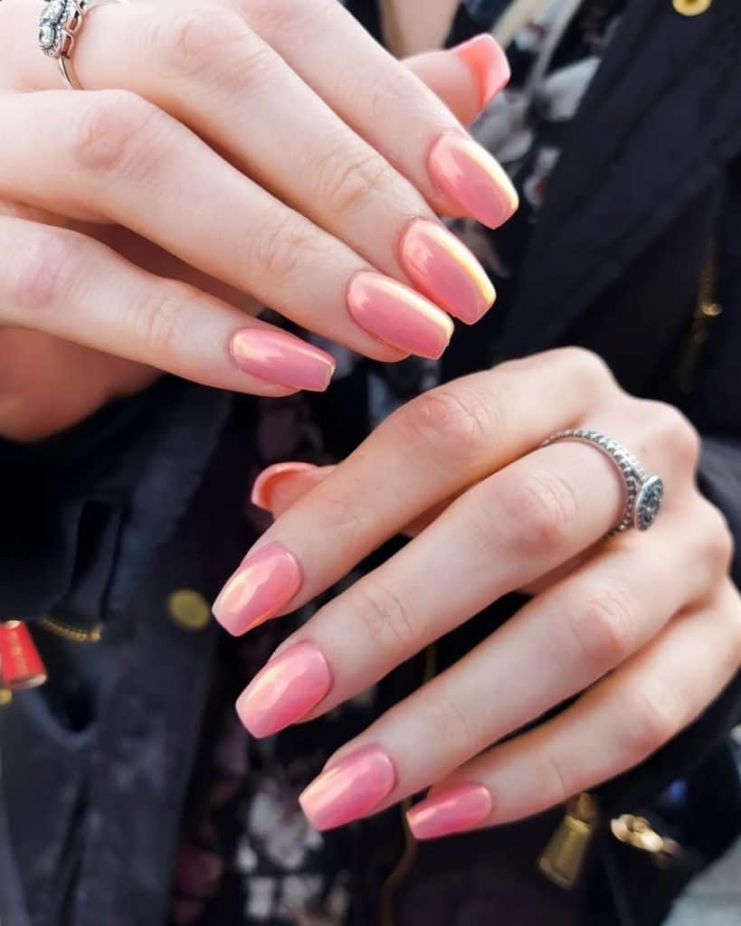 A woman with squoval nails with a stunning coral pink shade, merging the warmth of coral with the sleekness of a chrome finish