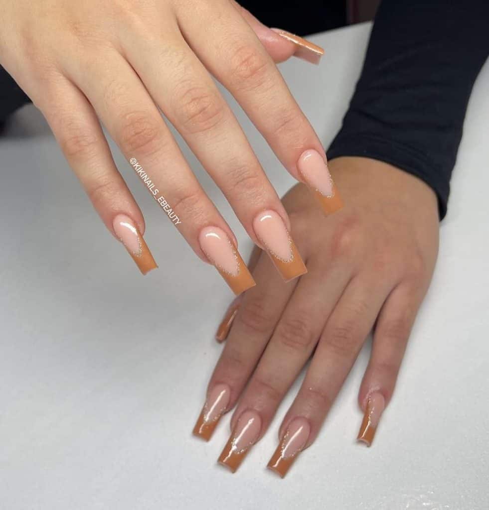 A woman's aesthetic nails showcasing caramel French tips outlined by thin silver glitter.
