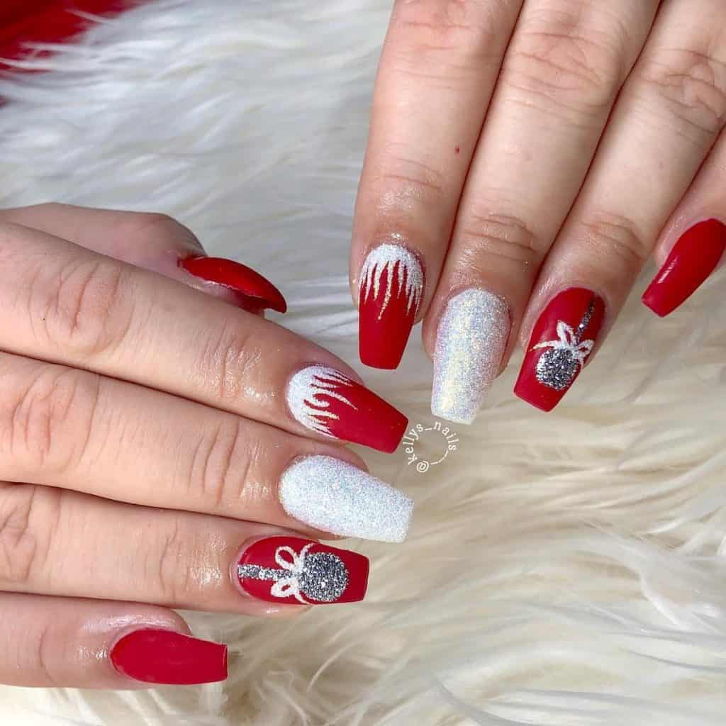A woman's short coffin-shaped matte red nails that sparkle with glittery silver Christmas balls and frosty icicles in white glitter near the cuticles.