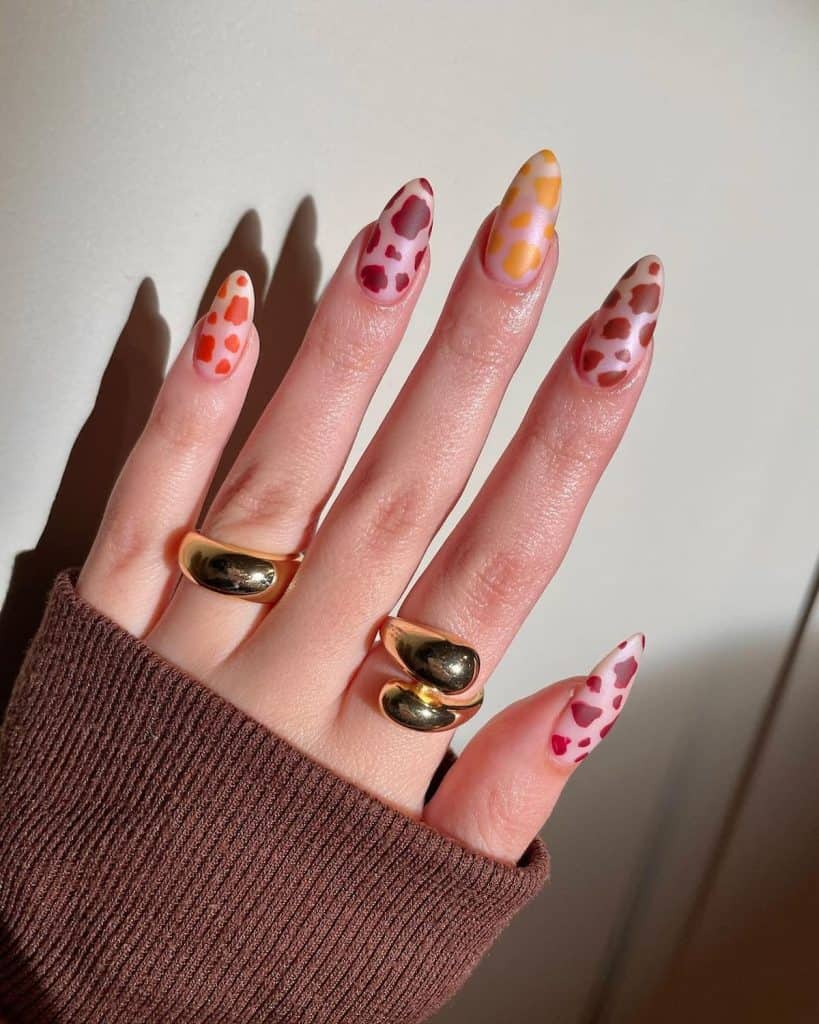 Matte nude nails in almond shape take a walk on the wild side with cow print patterns in vibrant yellow, orange, and red, adding a pop of fun to your fingertips.