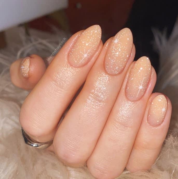 A woman's hand holding a beige glitter nail polish.