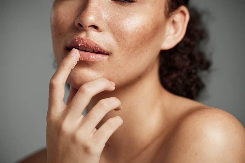 Happy female applying treatment for lip exfoliation